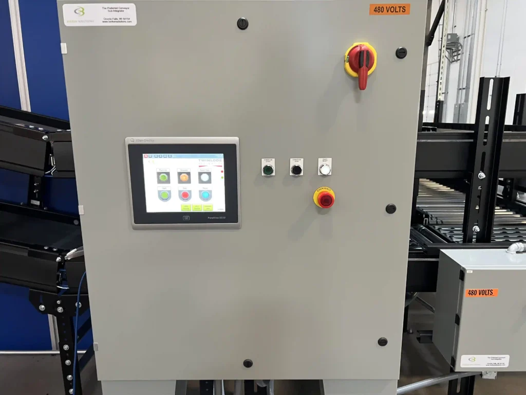 A conveyor control panel with a big red power switch in the upper right, a flat screen control panel in the middle left and an emergency stop button in the middle right.