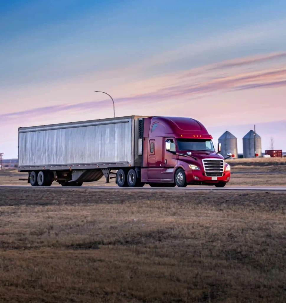 A red semi truck traveling through the country side.