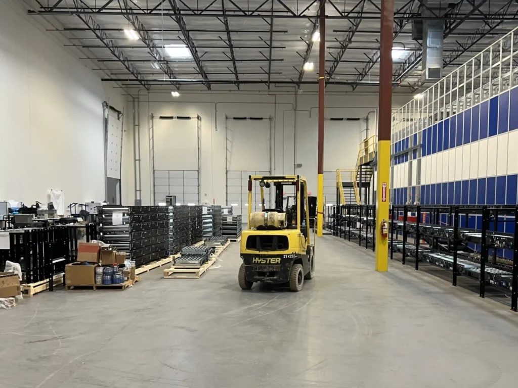 An installation of a conveyor system with the completed portion on the right; uninstalled components on the left; and a forklift in the middle.